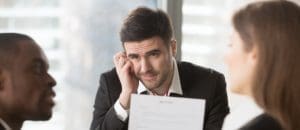 Worried male job candidate interested in company vacancy anxiously looking on multinational recruiters analyzing and discussing his resume on interview. Unconfident applicant waiting hiring decision