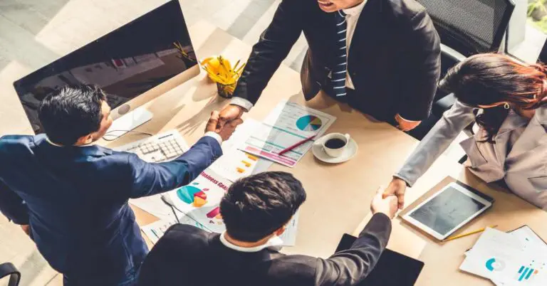 Post-merger integration, enterprise M&A, Group business people handshake at meeting table in office together with confident shot from top view . Young businessman and businesswoman workers express agreement of investment deal.